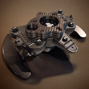 May include: A black and gray gaming controller with a carbon fiber center and multiple buttons. The controller has a PlayStation logo and the words "SHARE" and "PS" are visible. Two large paddle shifters are on the sides.