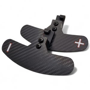 May include: A pair of black carbon fiber paddle shifters with a textured weave pattern. One paddle has a white line, the other a red plus sign. Each is attached with black screws.