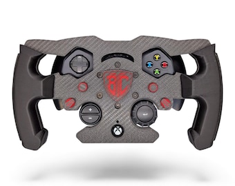 May include: A black carbon fiber racing steering wheel controller featuring a central red shield logo with the letters BC, a D-pad, four colored action buttons, two circular dials, and a small Xbox logo button at the bottom center.