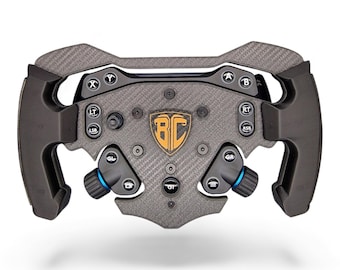 May include: A black carbon fiber racing steering wheel featuring a central shield logo with the letters BC in gold. The wheel includes multiple buttons labeled A, B, X, Y, LT, RT, LSB, RSB, GL, GR, and GT, along with two blue-accented rotary dials.