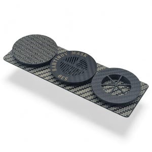 May include: A set of three dark gray Bahtinov masks, used for telescope focusing. The masks are made of a carbon fiber material and are arranged on a rectangular base with a chevron pattern. The central mask has the text "BAHTINOV MASK S30".