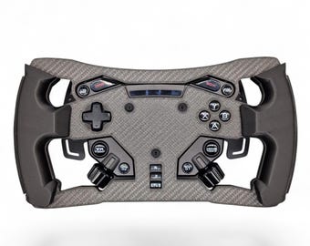 May include: A grey carbon fiber racing steering wheel controller featuring black rubberized grips, a directional pad, four action buttons labeled A, B, X, and Y, various function buttons including DRS and BOX, and a central display screen.