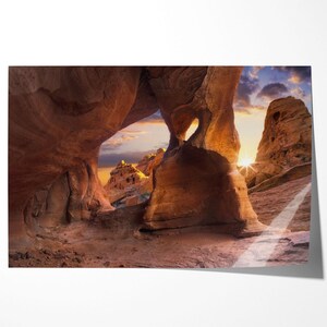 May include: A scenic photograph of a sandstone rock formation with a heart-shaped aperture. The image captures the warm colours of the setting sun, illuminating the rock face. The sky is a blend of orange, yellow, and blue, creating a dramatic backdrop.
