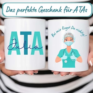 Könnte beinhalten: Zwei weiße Keramikbecher. Ein Becher zeigt die türkisfarbenen Buchstaben "ATA" mit dem Namen "Julia" in einer Schreibschrift. Der andere Becher hat eine Illustration eines medizinischen Fachangestellten mit dem Text "Bei mir liegst Du richtig!" und Daumen hoch.