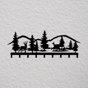 Puede incluir: Porta llaves de pared de metal negro con una silueta de una escena de bosque. La escena incluye montañas, árboles y dos ciervos. Hay ocho ganchos en la parte inferior del soporte.