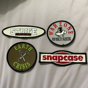May include: Four embroidered patches with various designs. The patches are white, gray, green, and red with black outlines. The patches feature the words "Strife", "Warzone", "Earth Crisis", and "Snapcase".