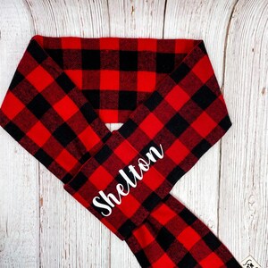 May include: Red and black buffalo plaid dog bandana with the name "Shelton" embroidered in white.