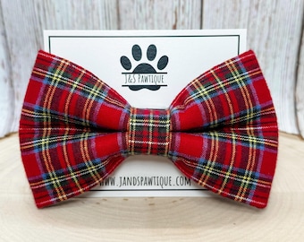 May include: Red and black plaid bow tie with yellow and blue accents. The bow tie is made of fabric and has a classic bow shape. The bow tie is on a white card with the text "J&S Pawtique" and "www.jandspawtique.com".