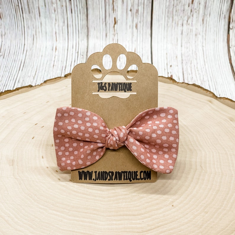 May include: A pink and white polka dot bow tie on a brown cardboard tag with the text "J&S PAWTIQUE" and "www.jandspawtique.com".