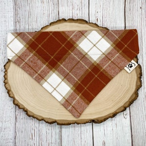 May include: A red, white, and tan plaid dog bandana with a small paw print logo.