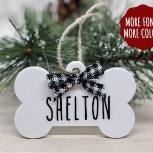 May include: White bone-shaped Christmas ornament with a black and white checkered ribbon and the name "Shelton" written in black.