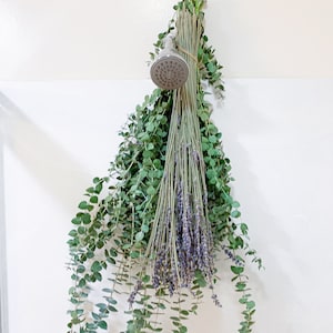 May include: A bunch of eucalyptus and lavender hanging from a shower head. The eucalyptus is green and the lavender is purple.