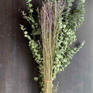 May include: A bouquet of dried lavender and eucalyptus tied together with a rubber band. The bouquet is on a dark wood background.