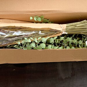 May include: A cardboard box filled with dried lavender and eucalyptus stems, a white cloth bag, and a small white box with a red cross.