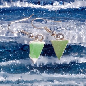 May include: A pair of drop earrings featuring triangular-shaped pieces of light green ceramic with a subtle crackle texture. Each piece is attached to a silver-toned metal hook with a small jump ring, creating a simple and lightweight design.