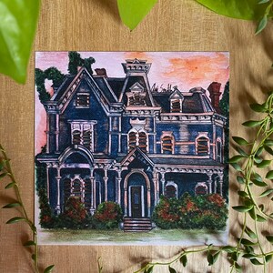K&ouml;nnte beinhalten: Aquarellmalerei eines dunkelblauen viktorianischen Hauses mit schwarzem Dach und wei&szlig;em Zierrat. Das Haus hat mehrere Fenster und eine Veranda. Der Himmel ist eine Mischung aus Rosa und Orange. Gr&uuml;nes Laub umgibt das Haus. Die Signatur des K&uuml;nstlers befindet sich in der oberen rechten Ecke.