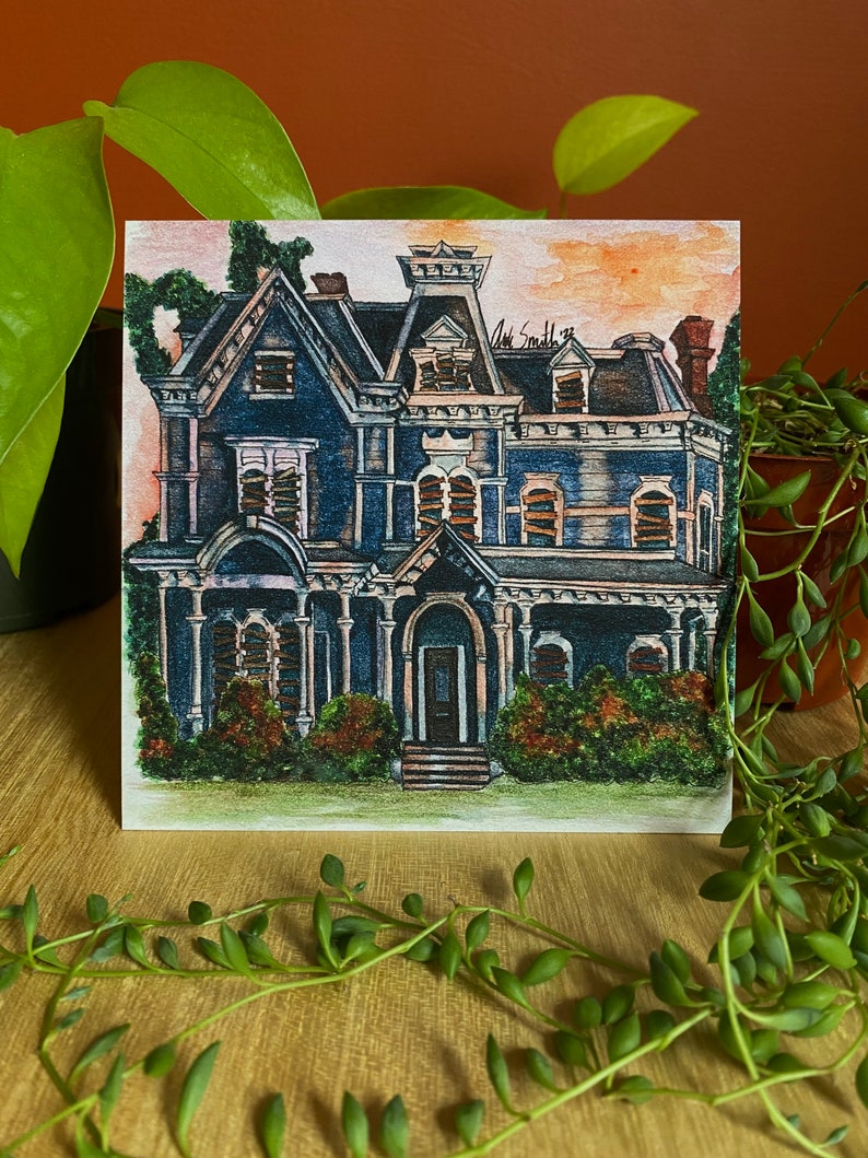 K&ouml;nnte beinhalten: Quadratischer Kunstdruck eines detaillierten blauen viktorianischen Hauses mit dunklem Dach und wei&szlig;en Zierleisten. Das Kunstwerk zeigt eine Veranda, mehrere Fenster und viel Gr&uuml;n. Die Signatur des K&uuml;nstlers, "Art Smith '22", ist oben rechts sichtbar.