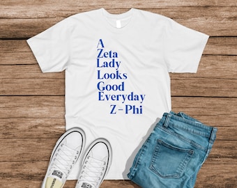 Puede incluir: Camiseta blanca con texto azul que dice "A Zeta Lady Looks Good Everyday Z-Phi".