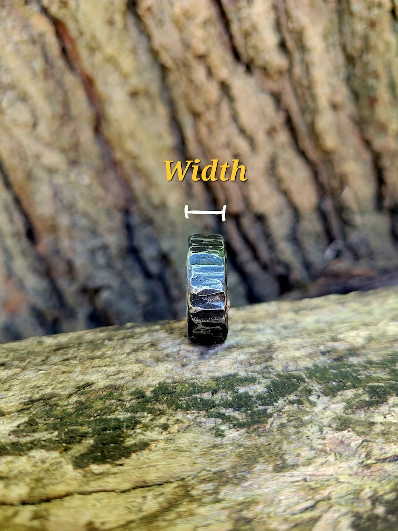 May include: A dark, textured ring with a hammered metal appearance. The ring is set against a natural wood background. The word "Width" is written in yellow above the ring.