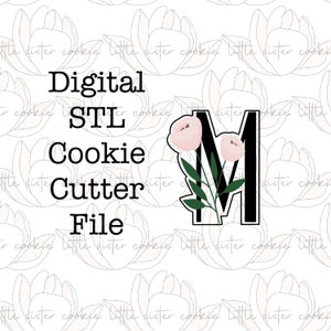 May include: Digital STL cookie cutter file. The design features the letter "M" with a floral motif. The letter is black with a white border, and the flowers are pale pink with green leaves. The background has a repeating floral pattern.