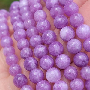 May include: Close-up of several strands of round, light purple beads. The beads have a smooth, polished surface and are strung together. The beads are a soft, muted shade of purple.
