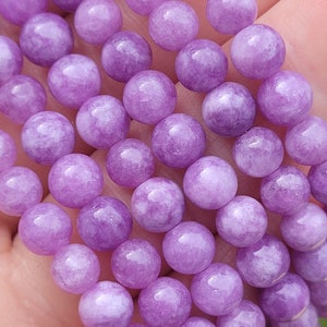 May include: Close-up of a strand of round, light purple beads. The beads have a smooth, polished surface and are strung together. The beads are a soft, pastel purple color.