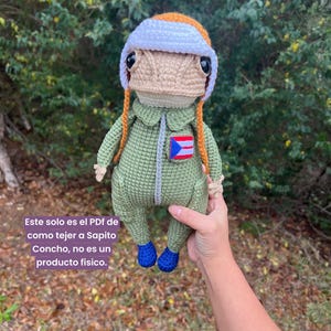 May include: A crocheted doll in a green jumpsuit, blue shoes, and a white and orange hat. The doll has a tan face and orange hair. The Puerto Rican flag is on the jumpsuit. Text on the image states this is a PDF pattern, not a physical product.