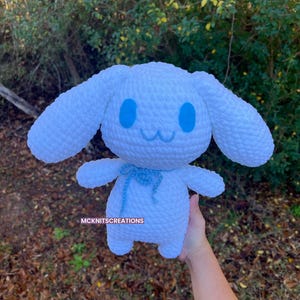 May include: White crocheted plush toy with blue eyes and a blue ribbon. The toy is shaped like a dog with floppy ears.
