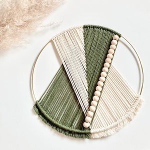May include: A circular wall hanging made of white and green yarn with wooden beads. The yarn is woven into a geometric pattern and the beads are strung along one of the lines.