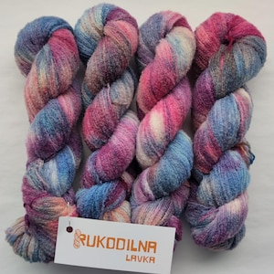 May include: Four skeins of hand-dyed yarn featuring a variegated blend of pink, blue, purple, and cream colors with a soft, fuzzy texture. A white rectangular tag is attached to the bottom left, displaying the orange text RUKODILNA LAVKA.