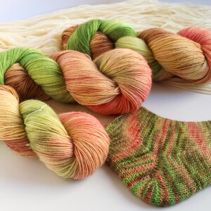 Può includere: Un primo piano di un gomitolo di filato in tonalità di verde, arancione e marrone. Il filato è disposto a spirale e i colori si fondono perfettamente. Il filato è perfetto per lavorare a maglia o all'uncinetto una varietà di progetti.