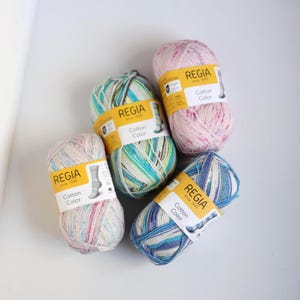 以下が含まれることがあります： 様々なパステルカラーのRegia Cotton Colorの毛糸玉が5つ。 ピンク、ブルー、グリーン、ホワイトなどの色が混ざっています。 各玉にはブランド名と製品情報が記載された黄色のラベルが付いています。 編み物や編み物プロジェクトに最適です。