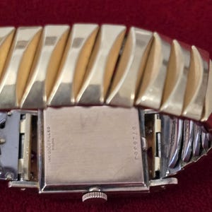 May include: Close-up of a vintage gold-filled Bulova watch. The watch features a rectangular face and a gold-toned, expandable band. The back of the watch is visible, with the inscription "14K Gold Filled Bulova" and the number "6726303".
