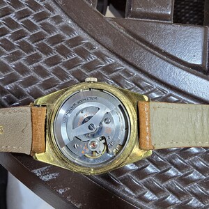 May include: A vintage gold-toned Waltham watch with a tan leather band. The watch's back is visible, showcasing the intricate mechanical movement and the inscription "WALTHAM WATCH CO."