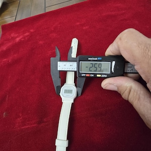May include: A white digital watch with a white band is measured with a digital caliper. The watch face displays the time. The caliper shows a measurement of 25.9 mm.