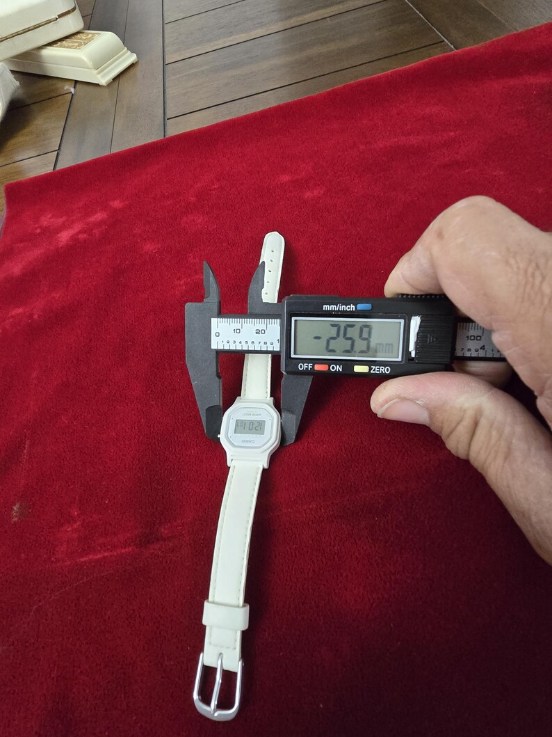 May include: A white digital watch with a white band is measured with a digital caliper. The watch face displays the time. The caliper shows a measurement of 25.9 mm.