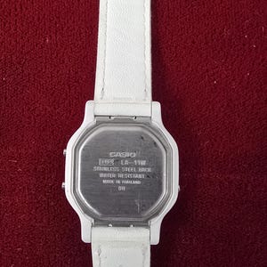 May include: A white Casio LA-11W digital watch with a white leather strap. The watch has a stainless steel back and is water resistant. The watch is made in Thailand.