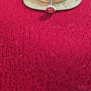 Pu&ograve; includere: Primo piano di un movimento di orologio con base dorata e ingranaggi argentati. La corona, con il logo Omega rosso, &egrave; visibile. Sfondo rosso strutturato.