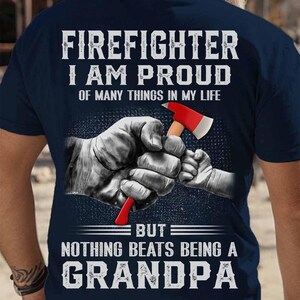 Peut inclure: T-shirt bleu marine avec un graphique de pompier et le texte "FIREFIGHTER I AM PROUD OF MANY THINGS IN MY LIFE BUT NOTHING BEATS BEING A GRANDPA".