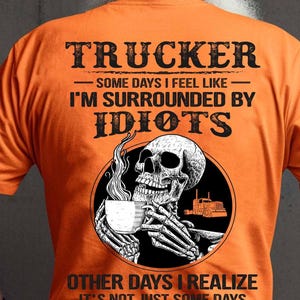 May include: Orange t-shirt with the text "TRUCKER" and a graphic of a skull holding a coffee cup. The shirt also has the phrases "SOME DAYS I FEEL LIKE I'M SURROUNDED BY IDIOTS" and "OTHER DAYS I REALIZE IT'S NOT JUST SOME DAYS".