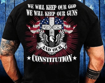 Może przedstawiać: Czarna koszulka z graficznym wzorem przedstawiającym krzyż z flagą amerykańską, orła i napis "WE WILL KEEP OUR GOD WE WILL KEEP OUR GUNS AND OUR CONSTITUTION". Projekt jest w kolorach czerwonym, białym i niebieskim.