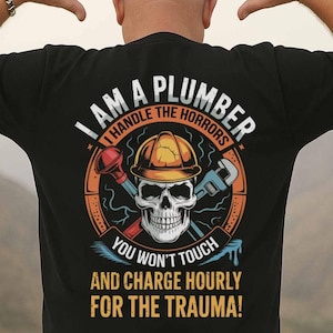 May include: Black t-shirt with a graphic featuring a skull wearing a hard hat, crossed tools, and the text "I AM A PLUMBER, I HANDLE THE HORRORS, YOU WON'T TOUCH, AND CHARGE HOURLY FOR THE TRAUMA!" in white and orange.