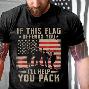 Op de afbeelding: Zwart T-shirt met een verweerd Amerikaans vlagontwerp en de tekst "IF THIS FLAG OFFENDS YOU, I'LL HELP YOU PACK." De afbeelding bevat silhouetten van soldaten. Ronde hals.