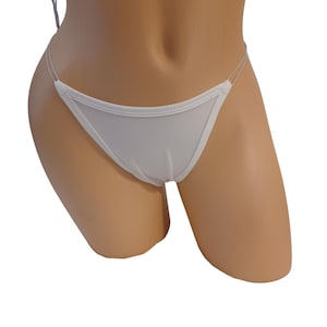 May include: A white thong featuring a smooth, opaque front panel with reinforced stitched edges and thin, translucent side straps. The garment is displayed on a neutral-toned mannequin torso, highlighting the minimalist design and clean lines of the piece.