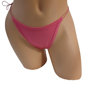May include: A solid pink bikini bottom featuring a low-rise cut with thin, double-string side ties. The garment has a smooth, matte finish and is constructed with visible stitching along the edges of the front panel and the delicate side straps.