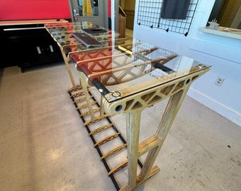 May include: A wooden table with a glass top and a black metal frame. The table has a unique design with a geometric pattern. The table is in a room with a red wall and a white wall.