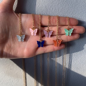 May include: A selection of butterfly pendant necklaces in shades of white, pink, blue, purple, orange, and green. Each necklace has a gold-coloured chain and clasp, displaying the butterfly charm.