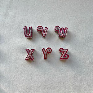 May include: Six silver charms with pink and white glitter letters spelling out the word "UVWXYZ".