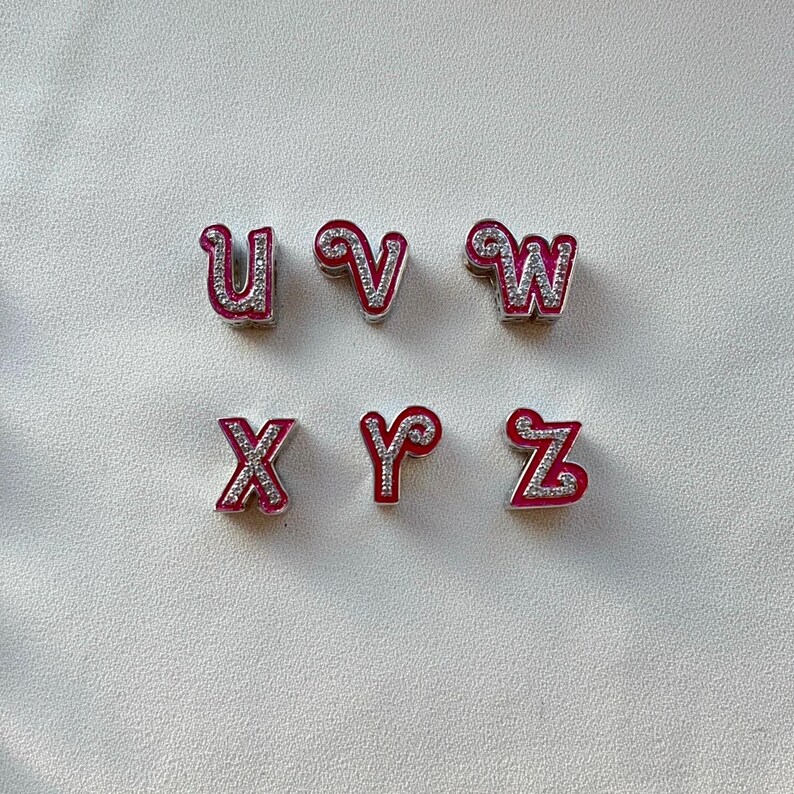 May include: Six silver charms with pink and white glitter letters spelling out the word "UVWXYZ".