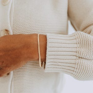 May include: A thin, flat gold-tone snake chain bracelet with a smooth, polished finish. The bracelet features a flexible, interlocking link design that sits flat against the wrist, creating a continuous, sleek, and reflective metallic band.